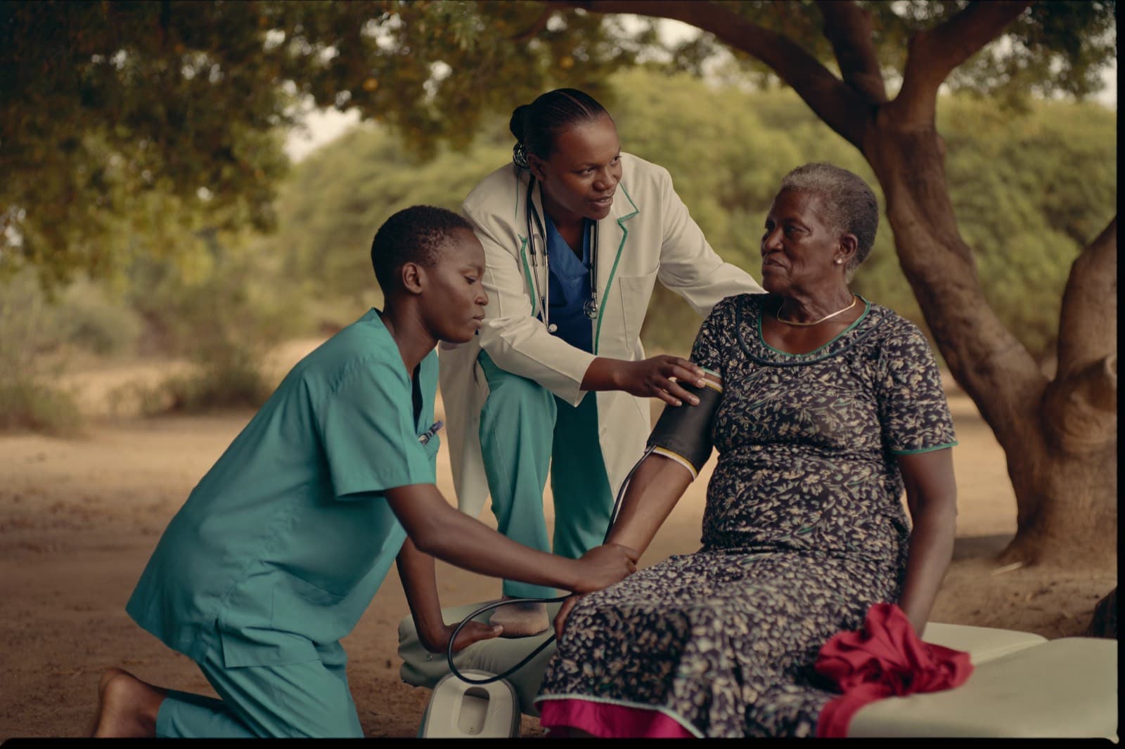 A medical student takes an elderly woman's blood pressure during community outreach while a mentor looks on